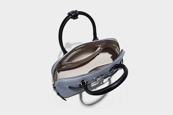 Compact structured satchel in light blue denim-look fabric with black leather-look trim, silver turn-lock closure, rolled