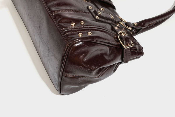 Glänzende Henkeltasche in Lederoptik mit zwei oberen Henkeln, goldfarbenen Nieten- und Ringbeschlägen, einem Riemendetail mit Schnalle auf der Vorderseite und