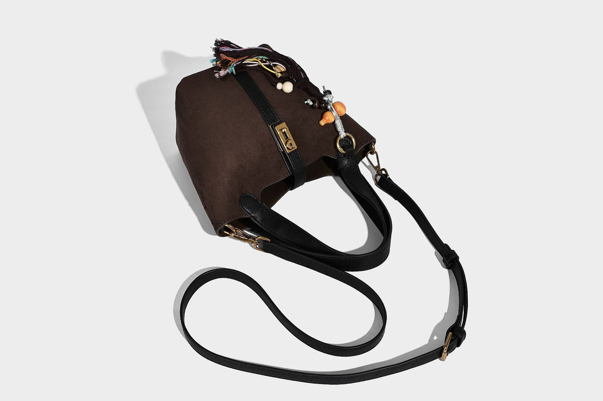 Small structured trapezoid tote bag in matte suede-look finish with black contrast trim, gold-tone front clasp, tassel charm