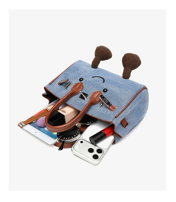 Small structured trapezoid satchel bag with smiling face motif, pom-pom accents, brown leather-look trim, silver-tone, detail
