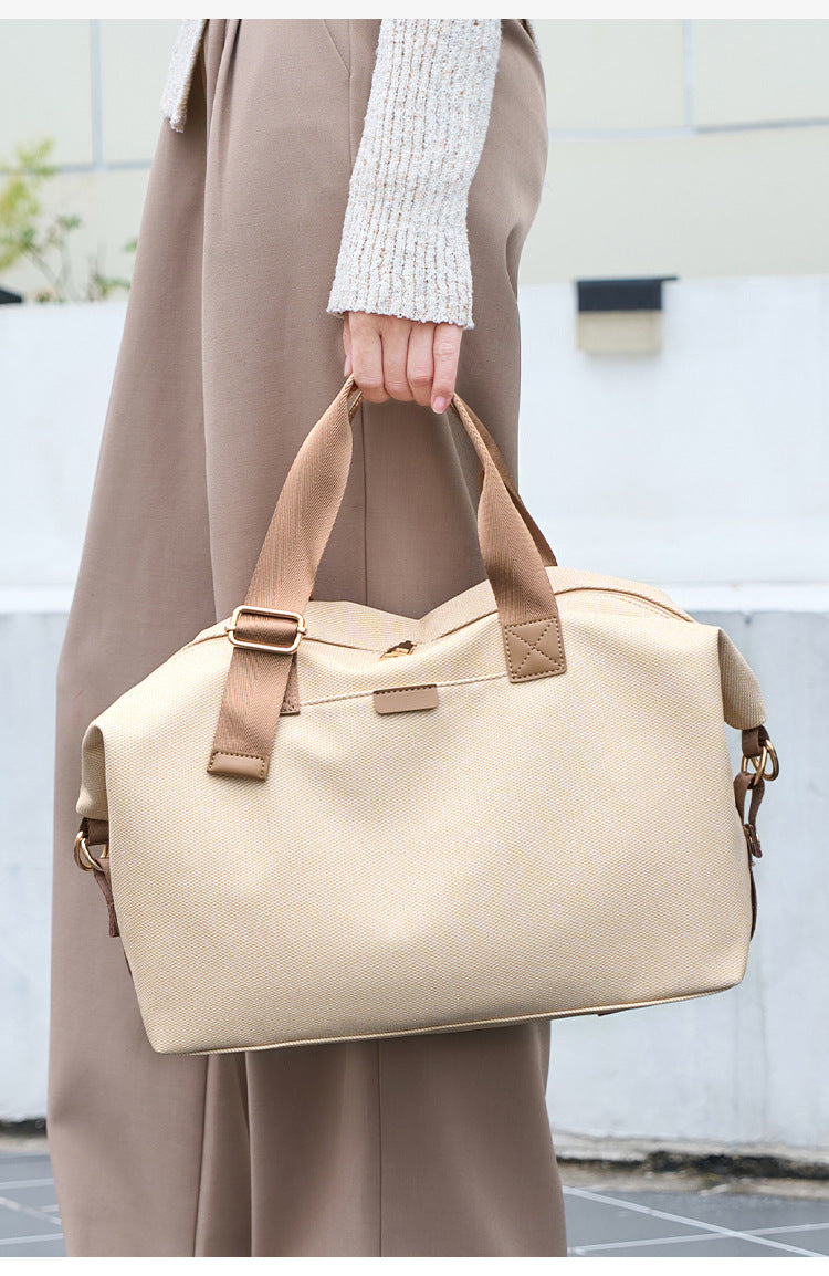 Structured woven duffel bag with dual tan webbing handles, detachable shoulder strap, top zip closure, and gold-tone