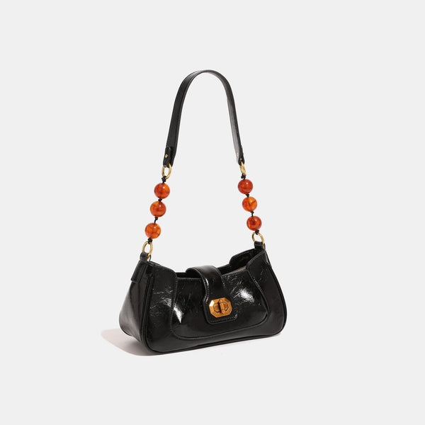 Compact glossy crinkled baguette shoulder bag with amber resin bead strap accent and gold-tone turn-lock closure, detail view