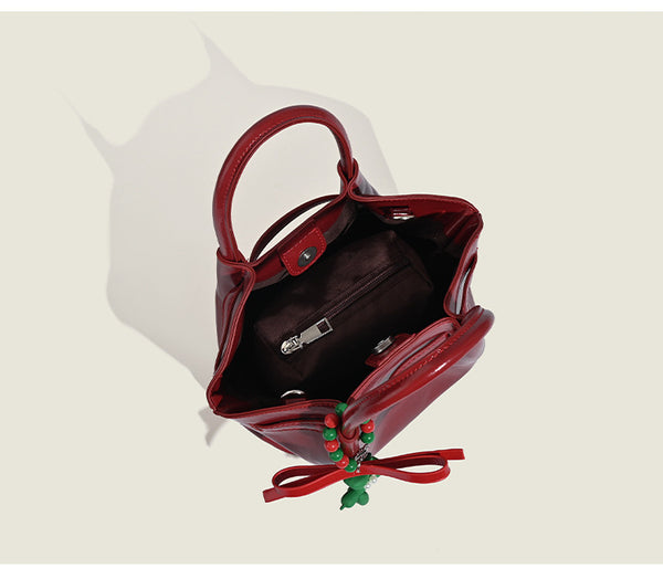Small structured red glossy PU handbag with bow-and-bead charm, dual top handles, and detachable crossbody strap, detail view