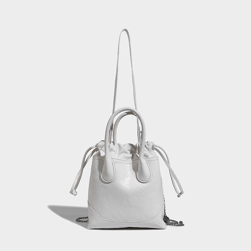 Glossy crinkled ruched drawstring bucket bag with rounded double top handles and detachable chain crossbody strap, detail
