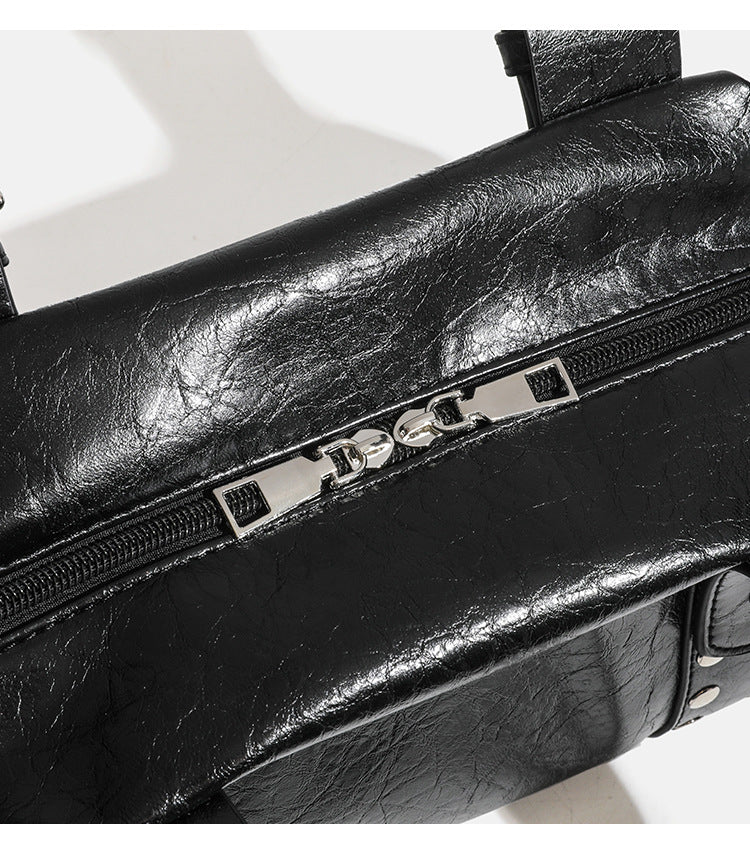 Compact black glossy leather-look satchel bag with silver-tone rivets, buckle hardware, and dual padded top handles, detail