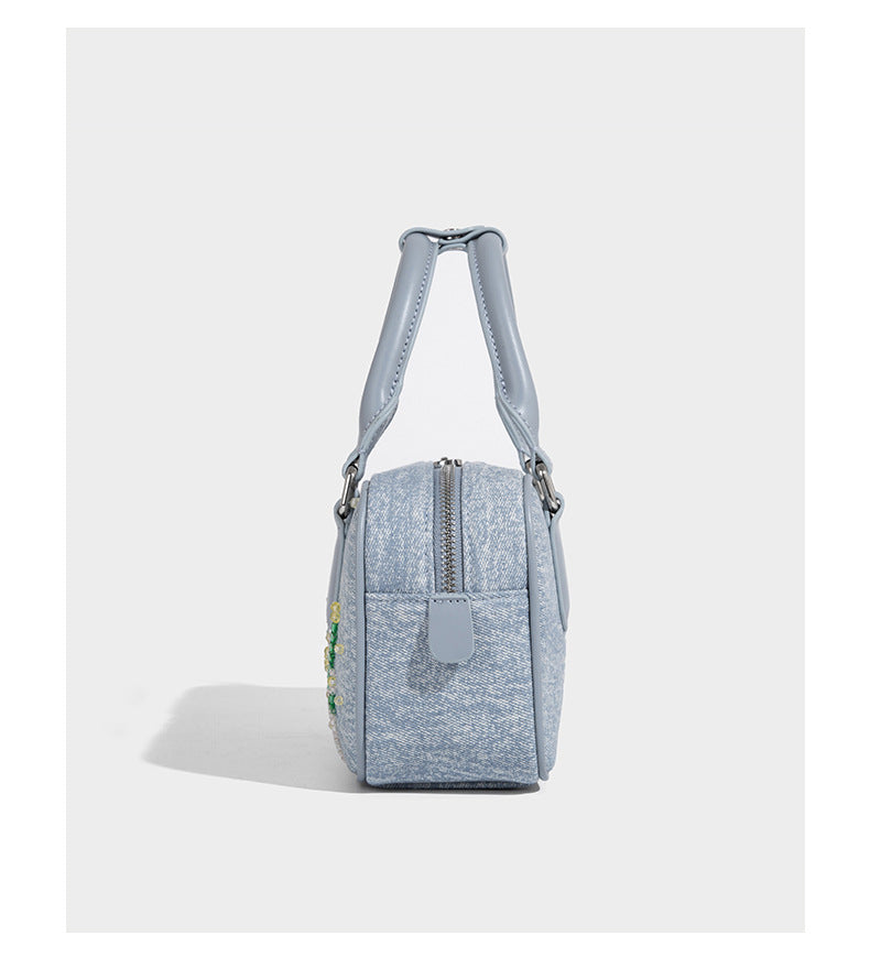 Small light blue denim-look barrel bag with white floral bead embroidery, dual top handles, and detachable shoulder strap