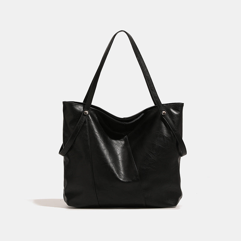 Große quadratische Shopper-Tasche in schwarzer Lederoptik mit zwei Schultergriffen und längerem Trageriemen, glatte glänzende Oberfläche und seitliche Beschläge