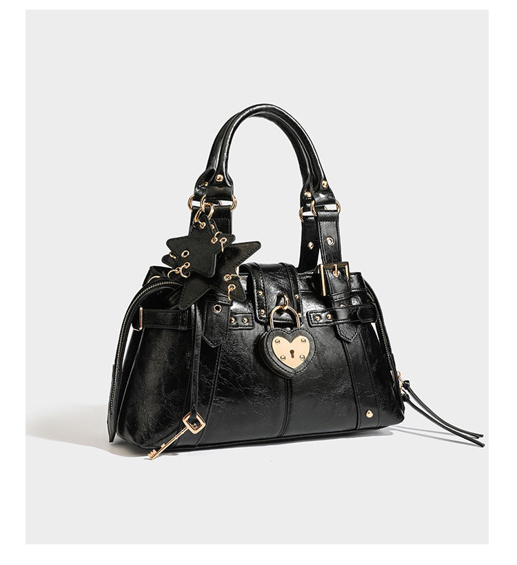 Structured leather-look satchel bag with heart padlock charm, star charm, gold-tone buckle hardware, dual top handles, and