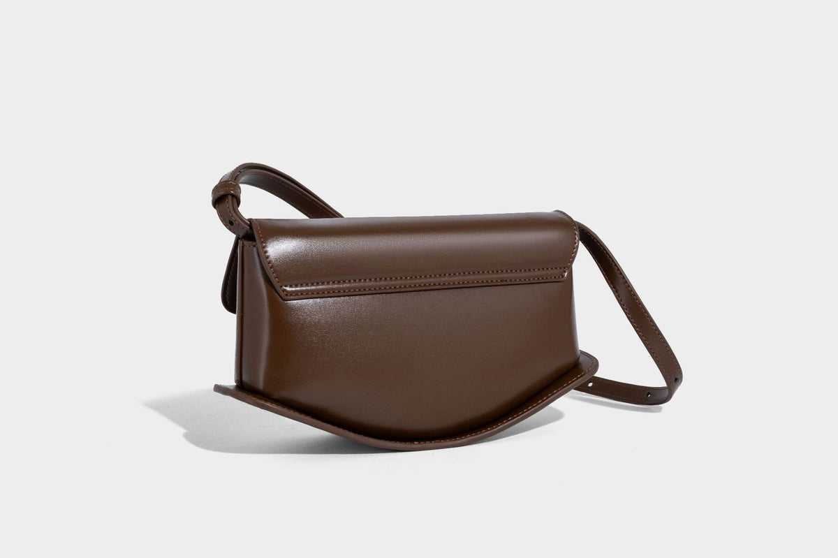 Small structured saddle bag with glossy leather-look finish, angular flap front, silver-tone metal clasp, and slim