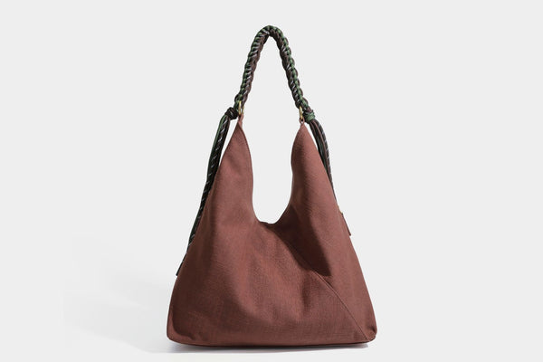 Soft slouchy cream canvas shoulder tote with braided brown and green cord handle, gold-tone ring hardware, and tassel trim