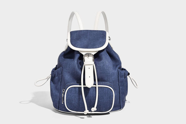 Compact denim drawstring backpack with white leather-look piping, flap-top buckle closure, front zip pocket, and silver-tone