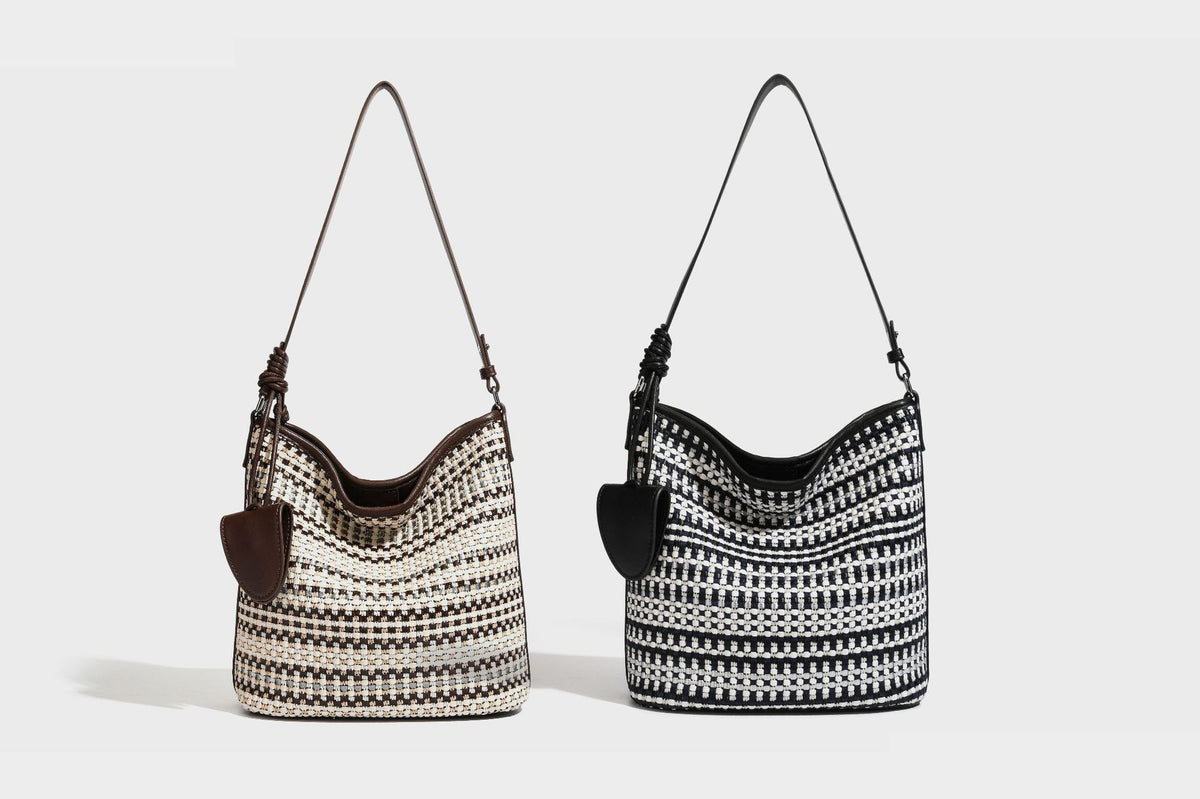 Woven stripe bucket shoulder bag in cream and dark brown with leather-look trim, knotted adjustable strap, and small shield