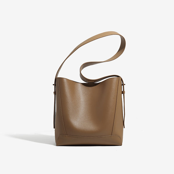 Structured smooth leather-look bucket shoulder bag with long adjustable strap and gold-tone buckle hardware in brown, detail