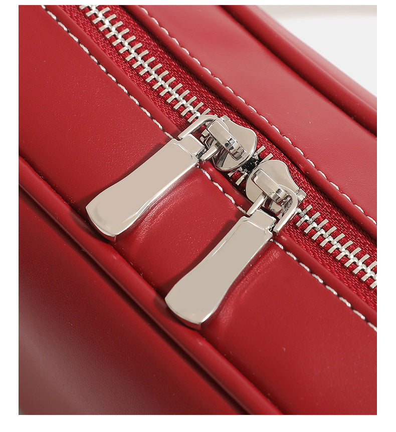 Compact rounded baguette shoulder bag with smooth leather-look finish, slim double straps, silver-tone zipper hardware, and