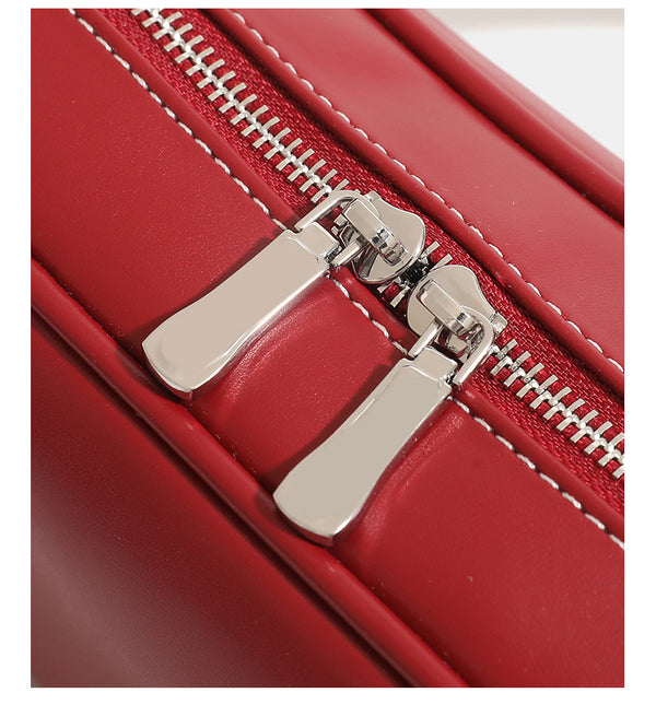 Compact rounded baguette shoulder bag with smooth leather-look finish, slim double straps, silver-tone zipper hardware, and