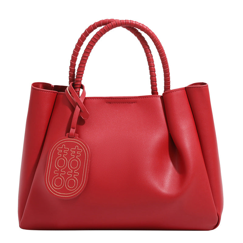 Strukturierte Tote-Bag in mattem Rot mit gedrehten, umwickelten Tragegriffen, Anhänger mit Doppelglück-Symbol und herausnehmbarem grauem Innenfach mit Reißverschluss