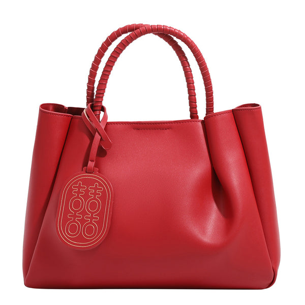 Strukturierte Tote-Bag in mattem Rot mit gedrehten, umwickelten Tragegriffen, Anhänger mit Doppelglück-Symbol und herausnehmbarem grauem Innenfach mit Reißverschluss