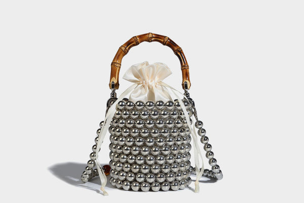 Small cylindrical bucket bag with glossy faux-pearl bead exterior, bamboo arched top handle, satin drawstring closure, and