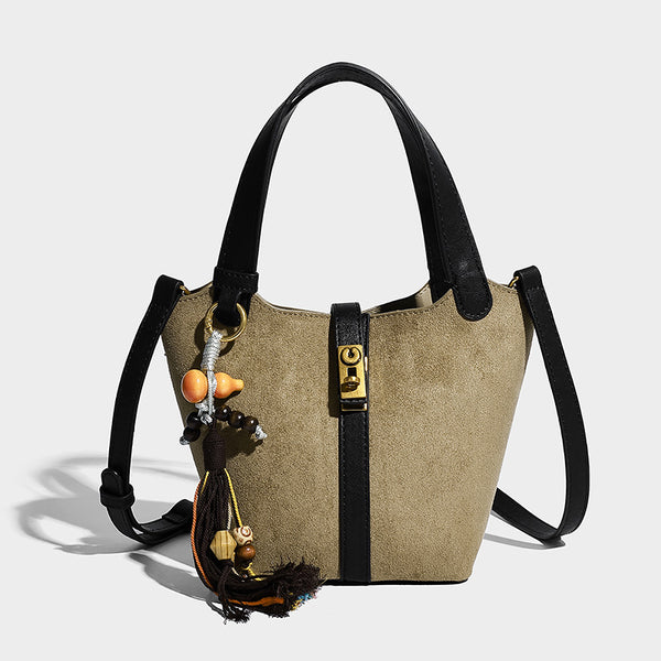 Small structured trapezoid tote bag in matte suede-look finish with black contrast trim, gold-tone front clasp, tassel charm