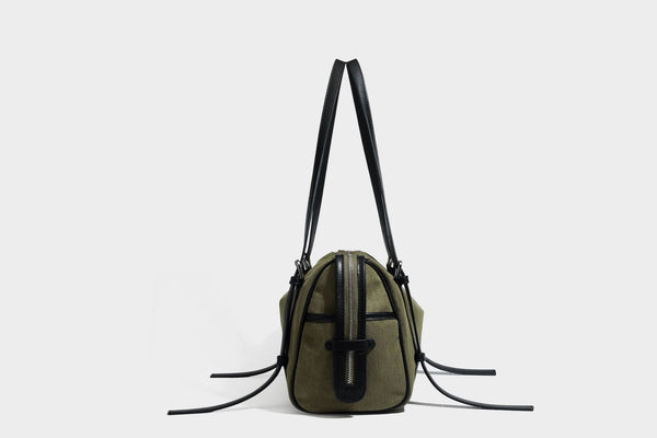 Olivgrüne Canvas-Schultertasche in Zylinderform mit schwarzen Trägern in Lederoptik, Reißverschluss oben und silberfarbenen Metallbeschlägen, Detailansicht