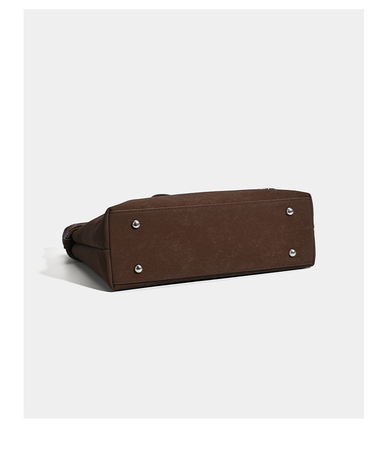 Brown structured tote bag with woven plaid fold-over top panel, silver-tone ring hardware, and long flat shoulder straps