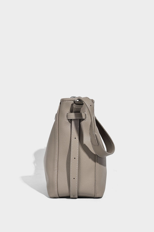Soft-structured pebbled bucket shoulder bag with front turn-lock strap detail, adjustable strap, and hanging floral tassel