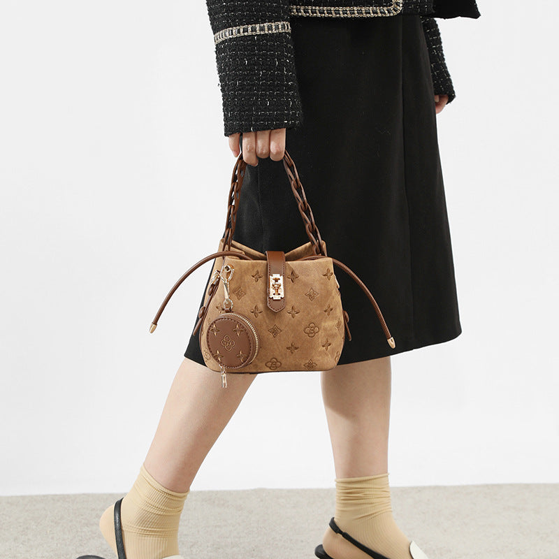 Compact monogram-embossed bucket bag with braided chain handle, gold-tone lock closure, and attached round coin pouch, detail