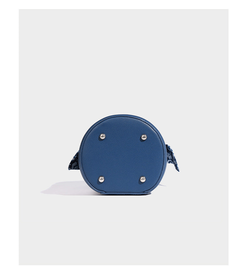 Small cylindrical barrel bag in blue-and-white floral jacquard with leather-look trim, scarf-wrapped top handle, silver-tone