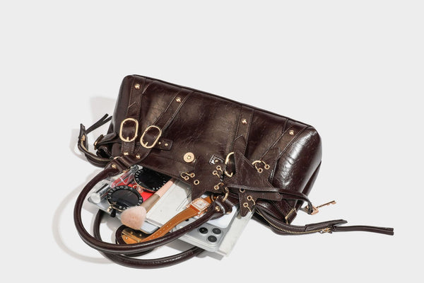 Glossy dark brown structured Boston satchel with heart-shaped lock charm, star pendant, rivet studs, multi-strap front panel