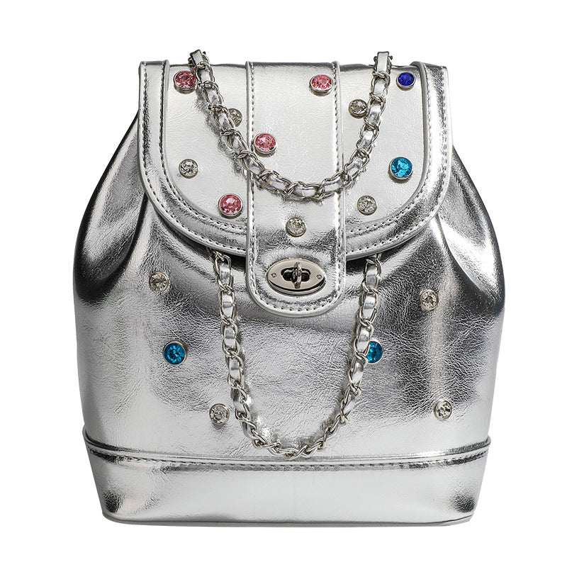 Kompakte silberfarbene Metallic-Rucksacktasche mit mehrfarbigen Kristallnieten, rundem Klappverschluss mit Drehverschluss und ineinander verflochtenem Silber
