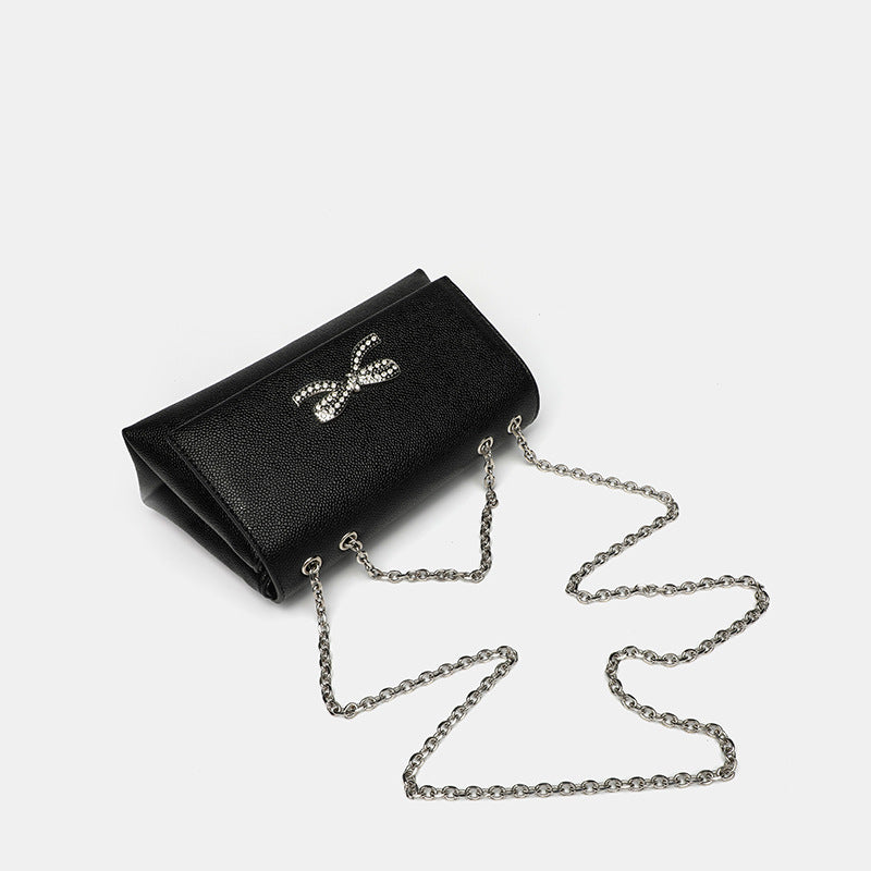 Structured rectangular flap crossbody bag with rhinestone bow and silver chain strap in pebbled finish, detail view 4