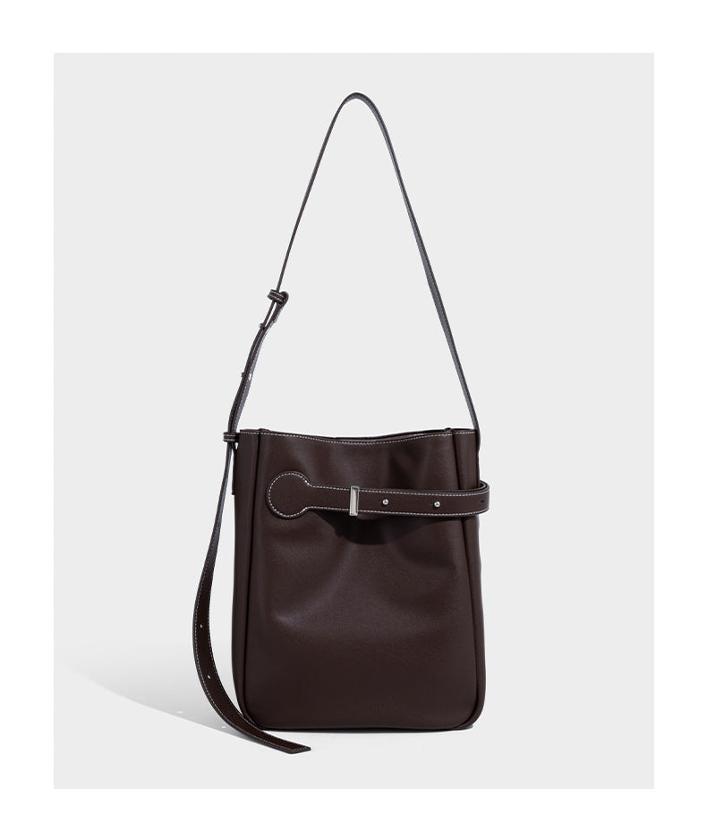 Structured dark brown leather-look bucket bag with white contrast stitching, front wraparound belt buckle strap, and long