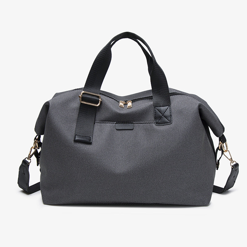 Structured woven duffel bag with dual tan webbing handles, detachable shoulder strap, top zip closure, and gold-tone