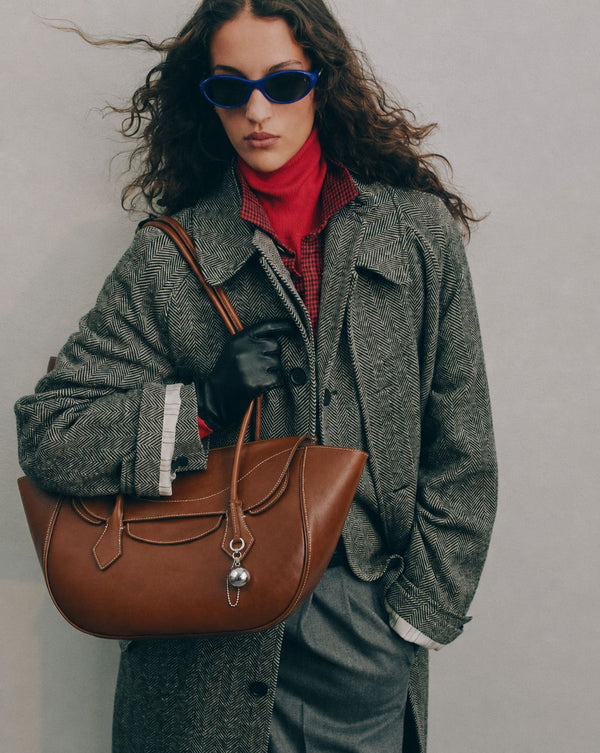 Large winged leather-look tote bag with single arched handle, stitched flap-front panel, and silver ball charm in cognac