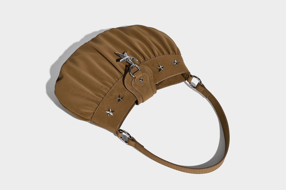Ruched shoulder bag with curved flap, silver star studs, dangling starfish charm, and adjustable crossbody strap, detail view