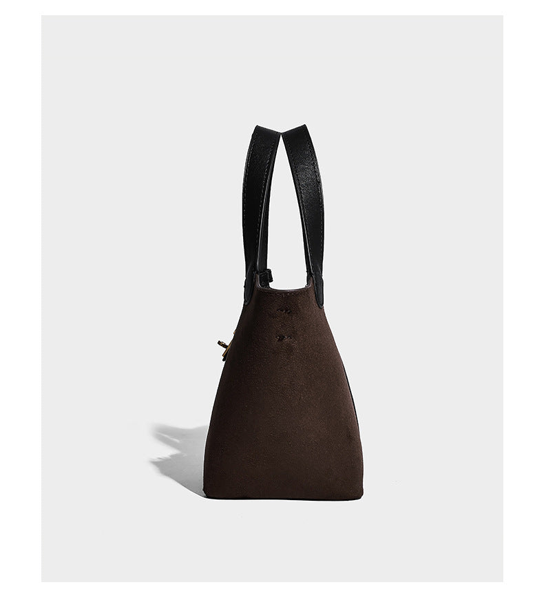 Small structured trapezoid tote bag in matte suede-look finish with black contrast trim, gold-tone front clasp, tassel charm