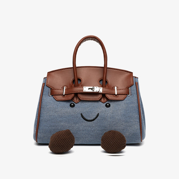 Small structured trapezoid satchel bag with smiling face motif, pom-pom accents, brown leather-look trim, silver-tone, detail