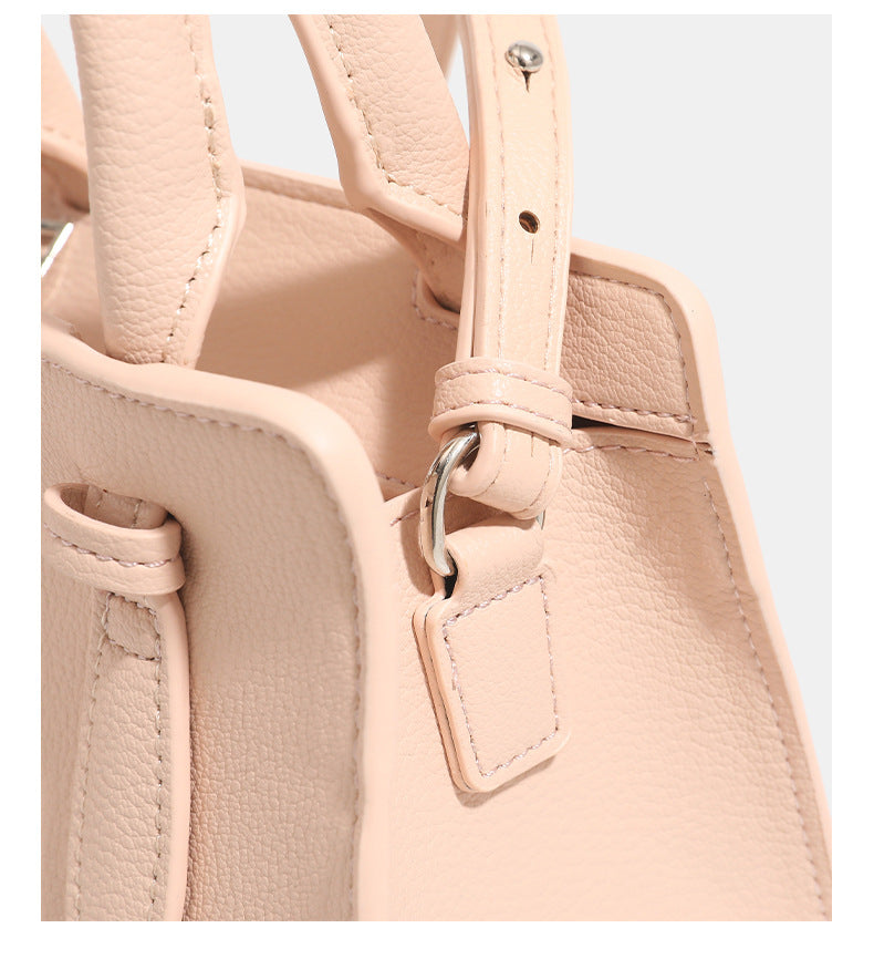 Small structured trapezoid top-handle bag in pebbled matte finish with decorative strap tabs, twin knotted handles, and