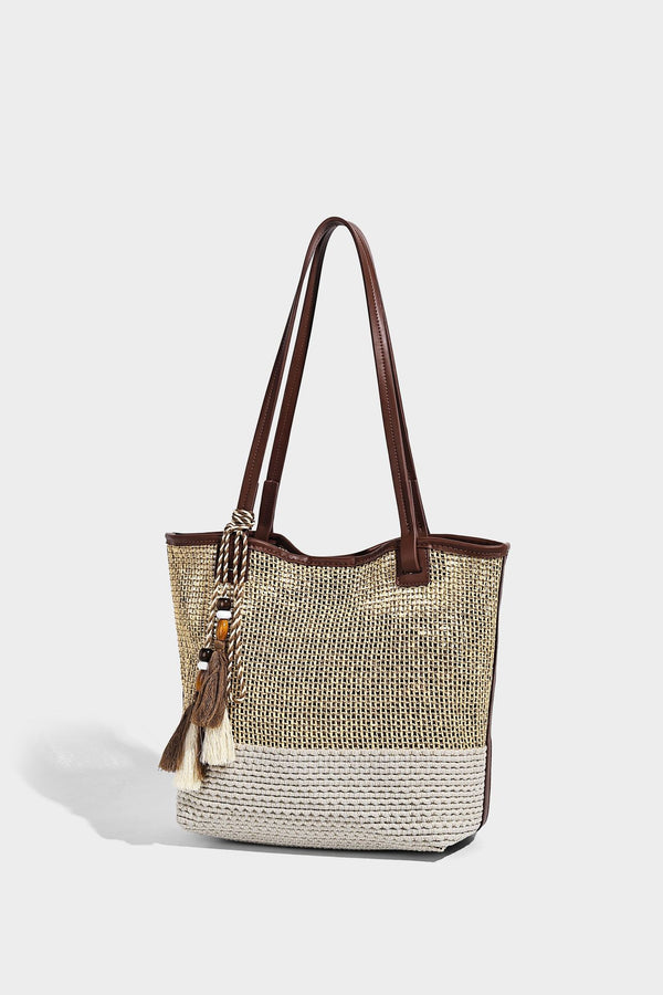 Woven beige and cream tote bag with brown leather-look trim, long double shoulder straps, and knotted tassel charm on front