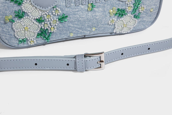 Small light blue denim-look barrel bag with white floral bead embroidery, dual top handles, and detachable shoulder strap