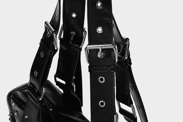 Glossy black crescent shoulder bag with silver-tone rivets, multiple zip pockets, and long adjustable studded straps, detail