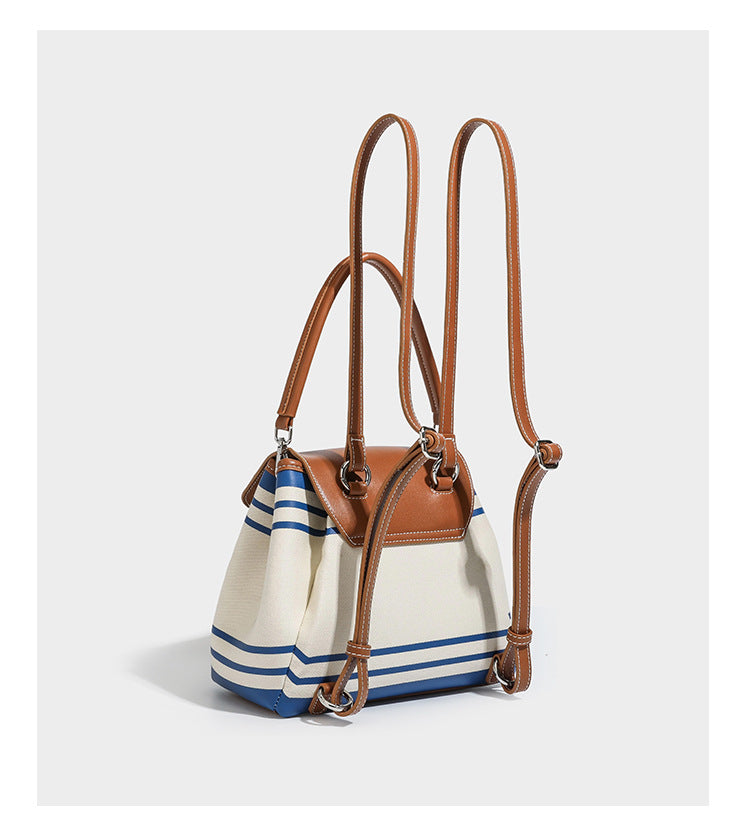 Cream canvas bucket bag with blue horizontal stripes, tan leather-look flap and trim, drawstring closure, silver-tone, detail