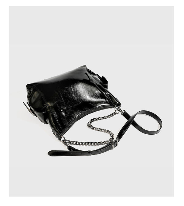 Slouchy hobo shoulder bag with glossy leather-look finish, silver-tone chain drape across front, side buckle pockets, and