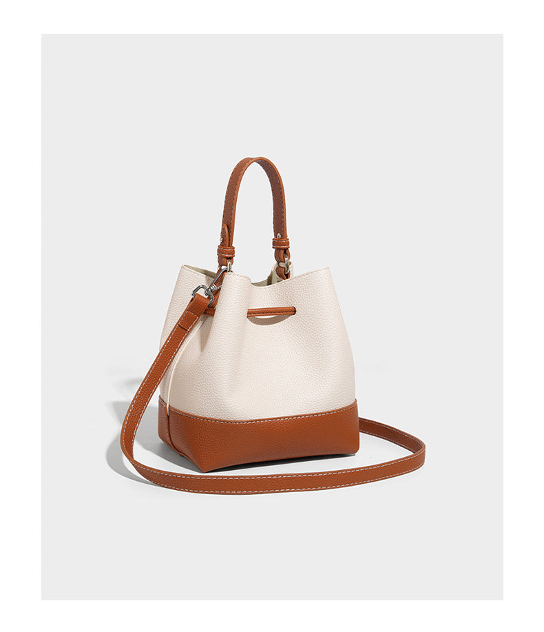 Small two-tone pebbled drawstring bucket bag with tan contrast base, metal toggle hardware, short top handle, and detachable