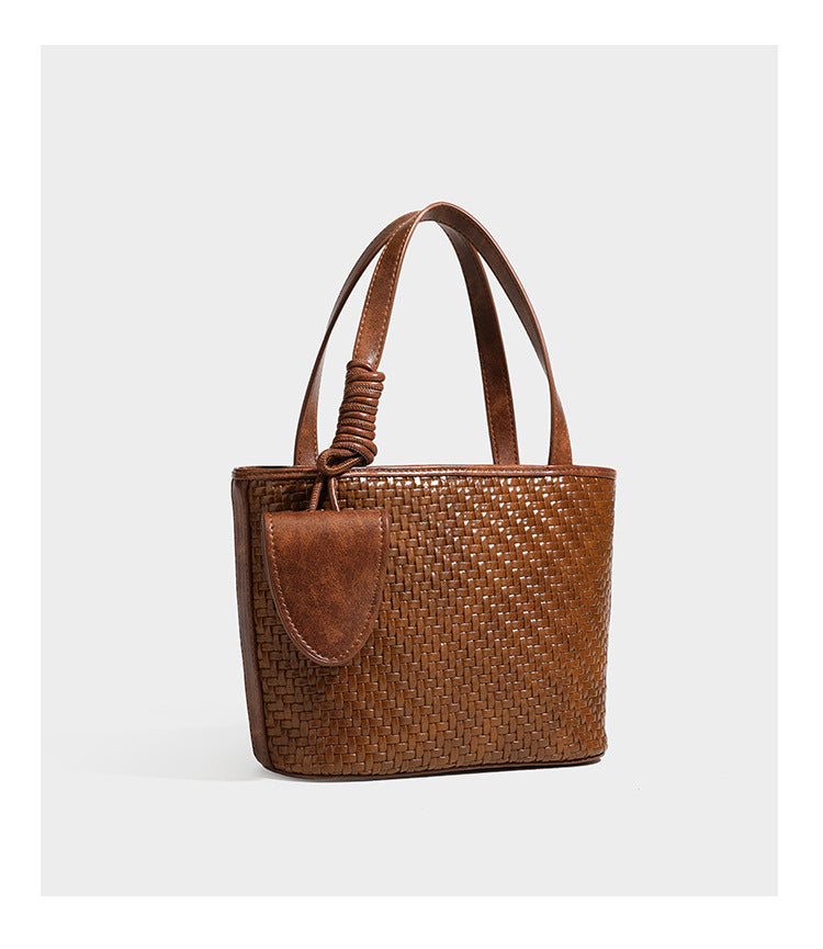 Strukturierte Tote Bag mit gewebter Oberfläche in Braun, goldfarbenen Metalldetails, seilumwickelten Tragegriffen, einer kleinen Fronttasche und weiteren Details