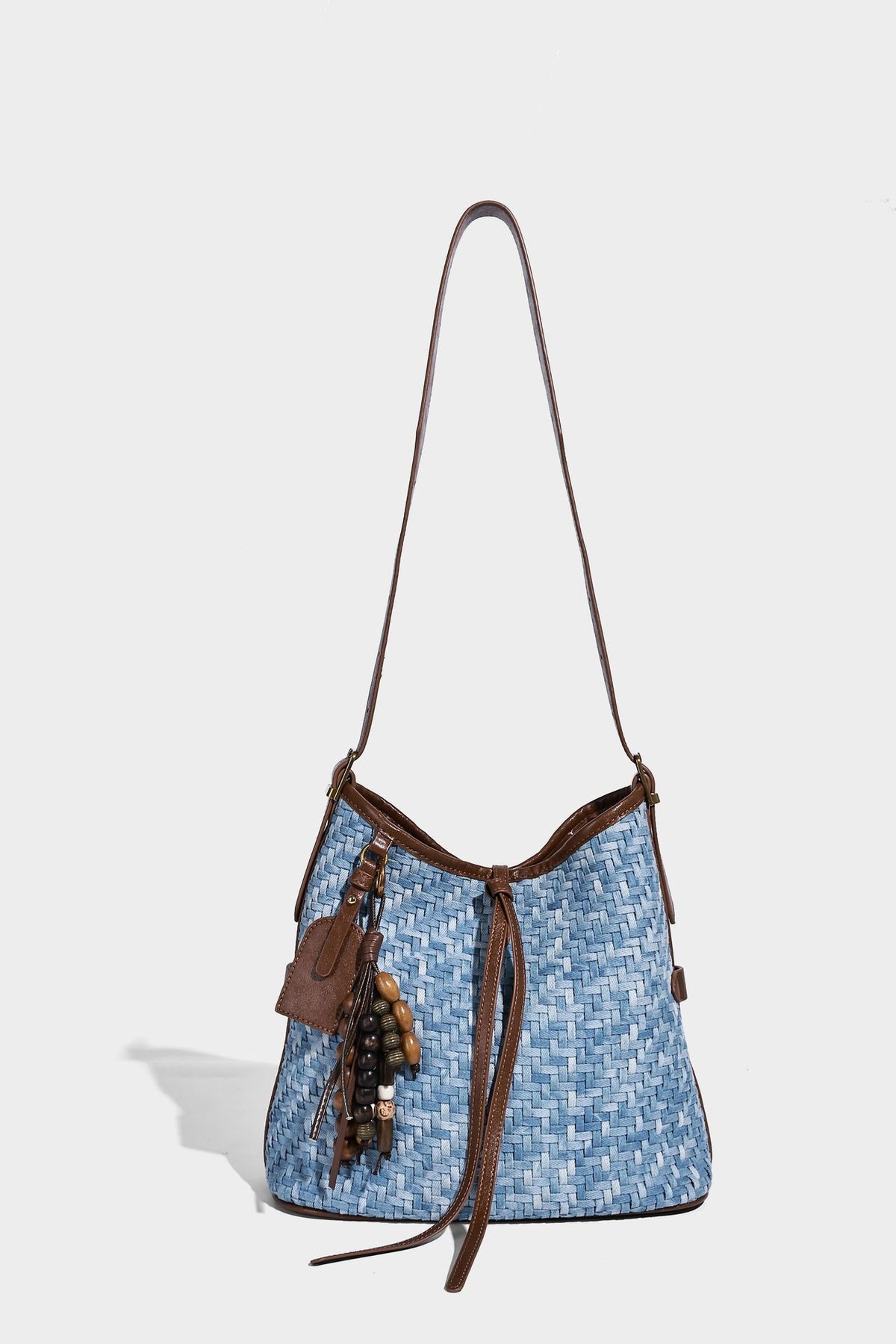 Light blue woven bucket bag with brown leather-look trim, gold-tone hardware, adjustable shoulder strap, and decorative bead