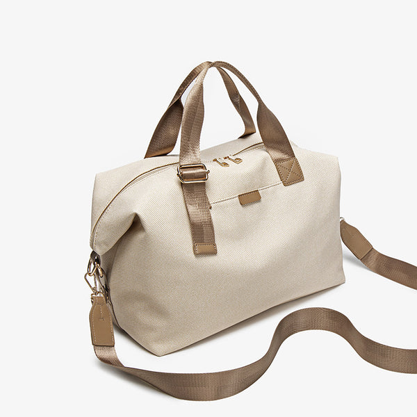 Structured woven duffel bag with dual tan webbing handles, detachable shoulder strap, top zip closure, and gold-tone