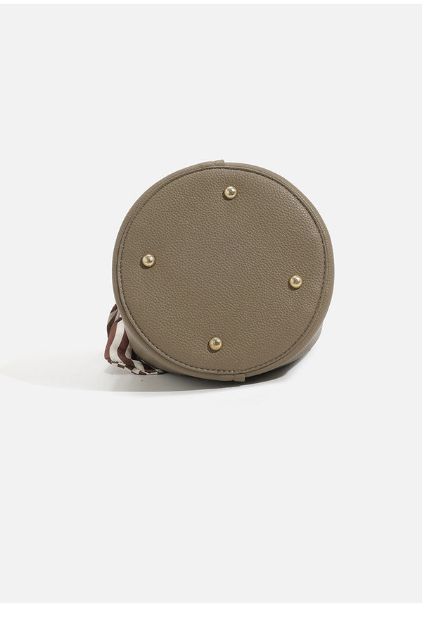 Pebbled leather-look bucket bag with checkered scarf-wrapped top handle, flap tab closure, gold-tone hardware, and matching