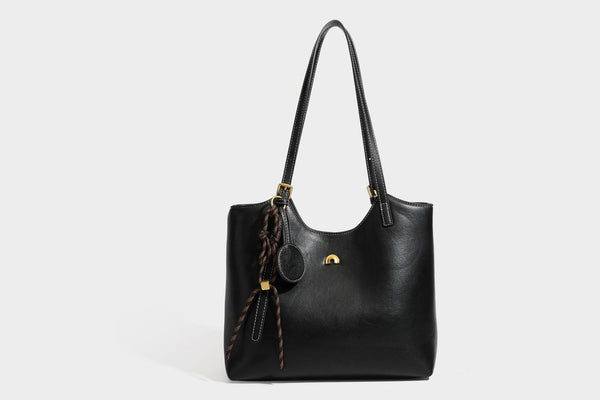 Structured smooth leather-look tote bag with long shoulder strap, gold-tone hardware, and hanging tassel-coin charm, detail