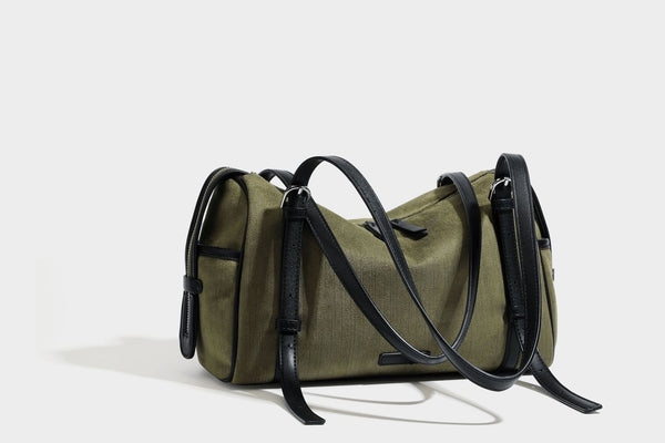 Olivgrüne Canvas-Schultertasche in Zylinderform mit schwarzen Trägern in Lederoptik, Reißverschluss oben und silberfarbenen Metallbeschlägen, Detailansicht